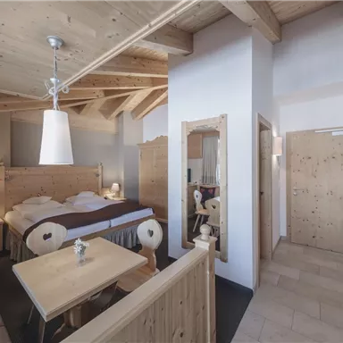 A cozy room with wooden decor and plenty of natural light. There is a table, chairs, and a large, comfortable bed.