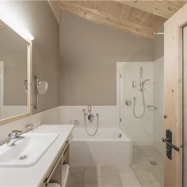 A modern bathroom with wooden walls and a large mirror. There is a shower and a bathtub, designed in a minimalist and stylish way.