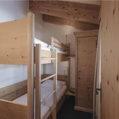 A cozy room with a wooden bunk bed and a wardrobe. The walls are light and the floor is dark, creating a pleasant atmosphere.