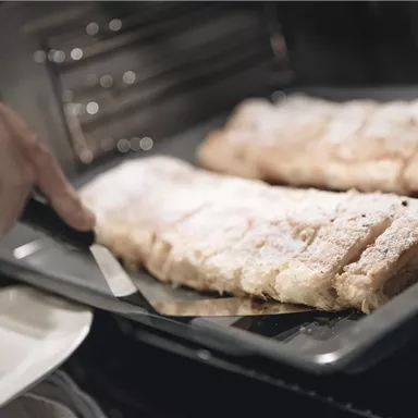 A plate with fresh pastries is taken out of the oven. The pastries are dusted with powdered sugar and look delicious.