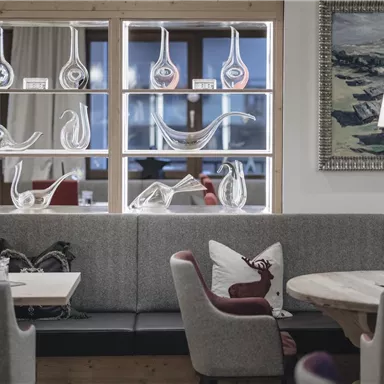 An elegant restaurant with cozy seating and a modern, stylish decor. Artistic glass objects are visible in the background.