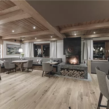 A cozy room with wooden floors and ceilings. In the center is a fireplace, surrounded by comfortable seating.