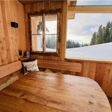A cozy, wood-paneled room with a round table. Outside is a snowy landscape with trees in the background.