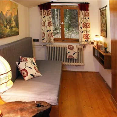 A cozy room with a gray bed and a lamp. The window offers a beautiful view and the walls are adorned with decorative curtains.