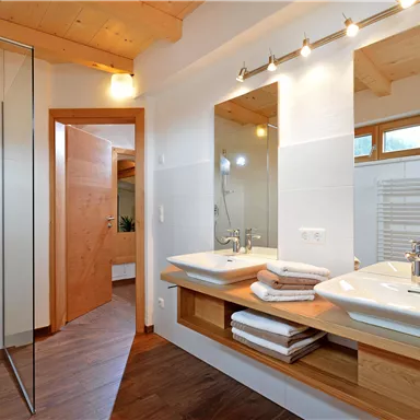 Ein modernes Badezimmer mit Dusche und doppeltem Waschbecken. Helles Holzdesign und große Spiegel sorgen für eine einladende Atmosphäre.