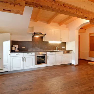 Eine moderne Küche mit weißen Schränken und Holzdecken. Der Boden ist aus Holz und es gibt eine kleine Pflanze im Raum.