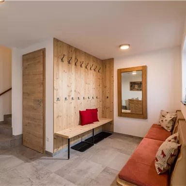 Ein moderner Flur mit Holzverkleidung und Garderobe. Es gibt eine bequeme Sitzbank mit roten Kissen und einen großen Spiegel.