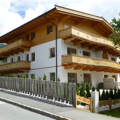 A modern house in alpine style with wooden balustrades and a well-maintained front garden. The surroundings are green and inviting.
