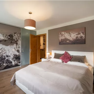 A modern bedroom with a large bed and a cozy atmosphere. A picture of the mountains is on the wall, and there is a glass wardrobe.