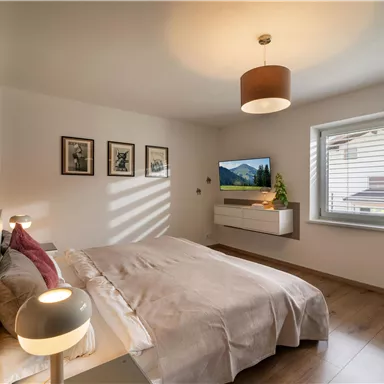 A modern bedroom with a double bed and soft lighting. Large windows provide daylight and a pleasant atmosphere.