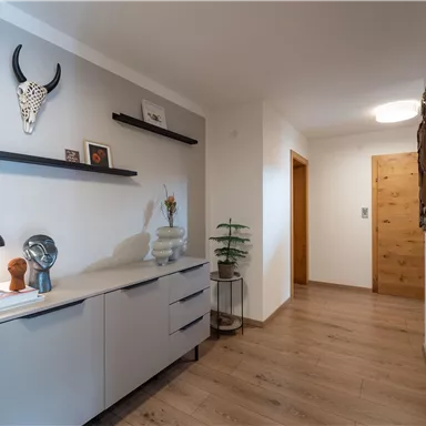 A modern hallway with a large mirror and a stylish dresser. The walls are light, and there are decorative elements as well as a wooden floor.