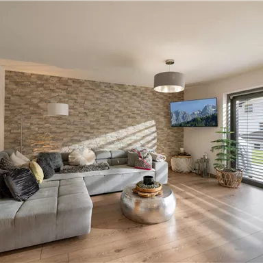 A modern living room with a comfortable couch and a round table.
Large windows let in plenty of light and a television displays a nature scene.