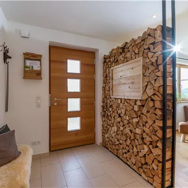 Ein moderner Eingangsbereich mit einer Holzverkleidung und einer großen Holzstapelwand. Die Tür ist aus Holz und hat mehrere Fenster.