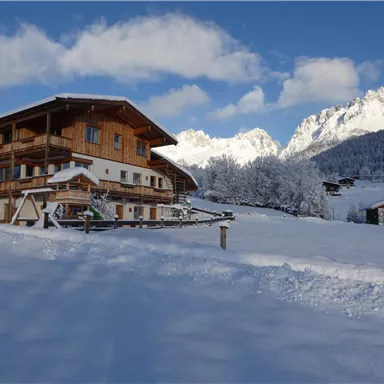 Ein charmantes Chalet inmitten einer verschneiten Landschaft. Im Hintergrund erheben sich majestätische Berge unter einem klaren Himmel.