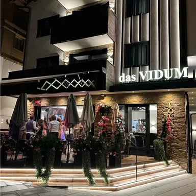 Ein elegantes Restaurant mit Außenbereich bei Nacht. Es sind Gäste anwesend, und der Eingang ist schön beleuchtet.