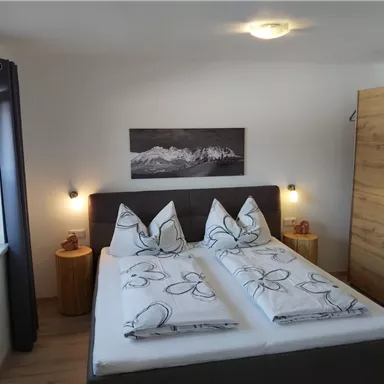 A cozy bedroom with a large double bed and decorative pillows. Pictures hang on the walls, and the room has a bright, inviting atmosphere.