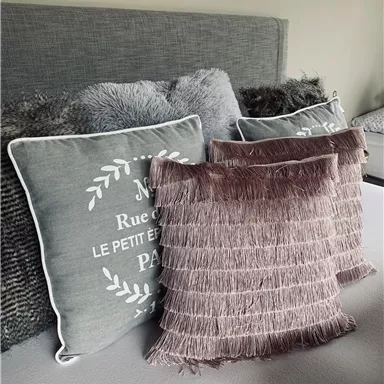 Ein gemütliches Bett mit mehreren dekorativen Kissen. Die Kissen haben verschiedene Texturen und Farben, die dem Raum eine einladende Atmosphäre verleihen.