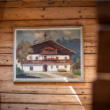 A painting of a traditional Bavarian house in a wooden frame. The picture is hung in a cozy wooden parlor.