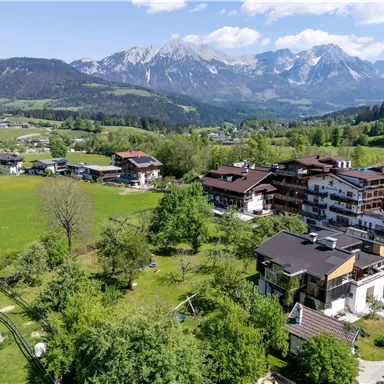 A picturesque landscape with green meadows and impressive mountains in the background. The surroundings are adorned with charming houses and trees.