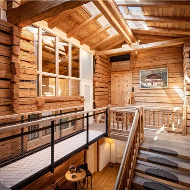A bright, modern wooden architecture with large windows and an open staircase area. The walls are made of visible wood, creating a cozy atmosphere.