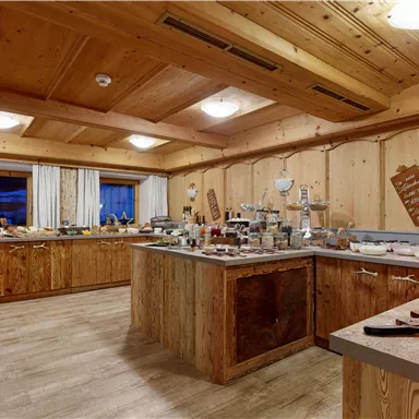 A cozy kitchen with wooden walls and an inviting atmosphere. Various foods and baked goods are arranged on the tables.