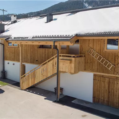 A modern wooden building in a snow-covered landscape. The structure has a balcony and a bright facade.