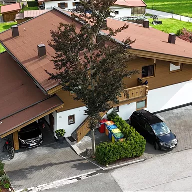 A large, two-story house with a brown roof and green lawns. Parking spaces are available directly in front of the house.