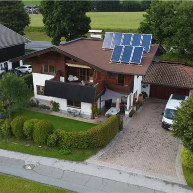 A modern house with solar panels on the roof. The garden is well-maintained and the surroundings are green.