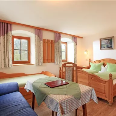 A cozy room with two beds and a blue sofa. The windows let in a lot of light and the decor features wood and natural colors.