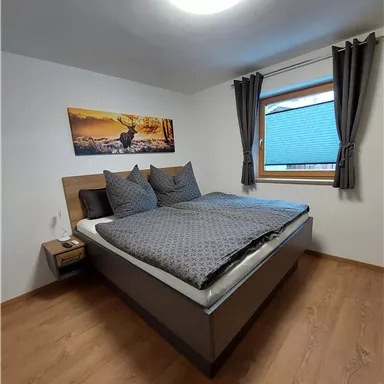 Ein modernes Schlafzimmer mit einem großen Bett und gemütlichen Kissen. Das Zimmer hat einen hellen Holzfußboden und ein Fenster mit Vorhängen.
