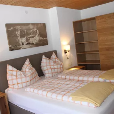 A cozy bedroom with a double bed and modern wooden details. In the background, a large bookshelf is visible.