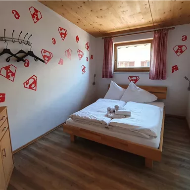 A cozy bedroom with a double bed and colorful wall designs. The windows let in plenty of daylight and create an inviting atmosphere.