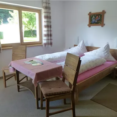 A cozy room with a double bed and a table. The windows let in a lot of light, and the space feels inviting and friendly.