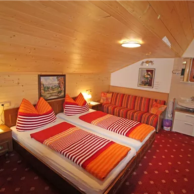 A cozy bedroom with two beds and orange pillows. The walls are made of wood, and there is a seating area as well as a bathroom.