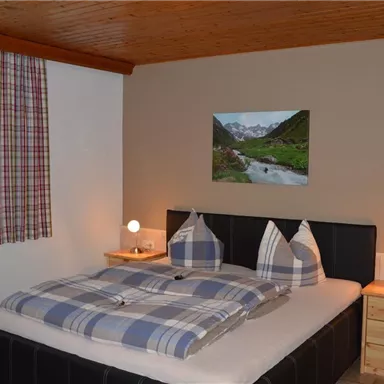 A cozy bedroom with a large bed and plaid bedding. There are pictures hanging on the walls, and there are table lamps on the nightstands.