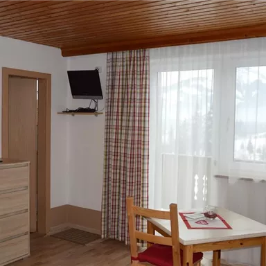 A cozy living space with a table and chairs. Through the window, there is a view of the mountains and the natural surroundings.