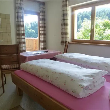 A simple room with two beds and a chair. The room has a window overlooking the green landscape outside.