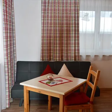 A cozy living space with a table and two chairs. The walls are clad in wood and the windows have curtains with a checkered pattern.