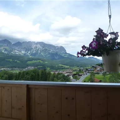 A beautiful landscape with mountains in the background and a hanging plant pot. In the foreground, a wooden balcony is visible.