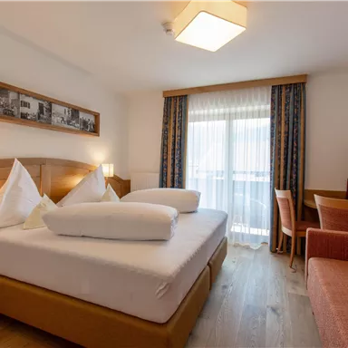 A cozy hotel room with a large bed, a desk, and a seating area. Large windows let in plenty of light and provide a view outside.