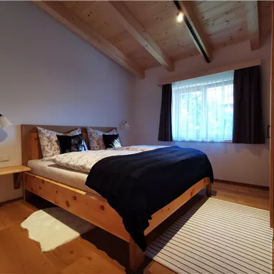 A cozy bedroom with a wooden bed and soft pillows. Natural light streams through the window, illuminating the space.