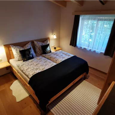 A cozy bedroom with a double bed and elegant bedding. A window lets in soft light, while dark curtains provide a beautiful contrast.