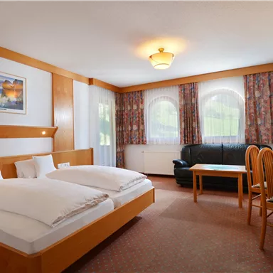A cozy hotel room with two beds, a television, and a seating area. Large windows provide plenty of natural light.