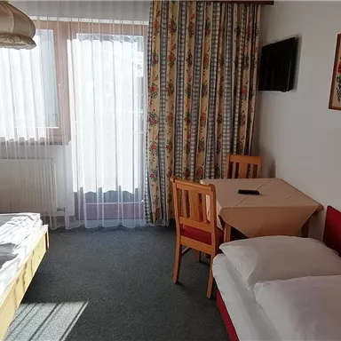 A cozy hotel room with two single beds and a table. Large windows provide plenty of daylight.