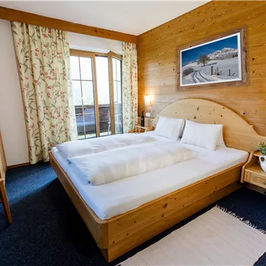Ein gemütliches Schlafzimmer mit einem großen Bett und Holzoptik. Das Zimmer hat Fenster mit Aussicht und eine einladende Atmosphäre.