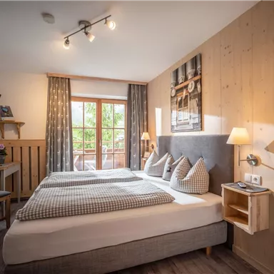 A cozy bedroom with a double bed and stylish decor. Large windows provide plenty of daylight and a view outside.