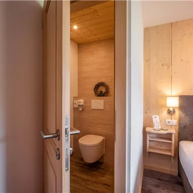 A stylish room with a modern bathroom and a cozy bed. The wood paneling creates a warm atmosphere.