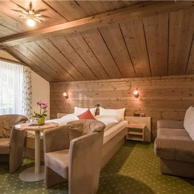 A cozy room with wooden ceilings and a double bed. There is a small table with chairs and a comfortable seating area.