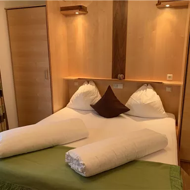 A cozy bedroom with a double bed and soft pillows. The wooden furniture creates a warm atmosphere.