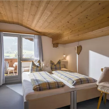 Ein gemütliches Schlafzimmer mit einem Doppelbett und Holzdecke. Blick auf den Balkon mit Aussicht auf die umliegende Landschaft.